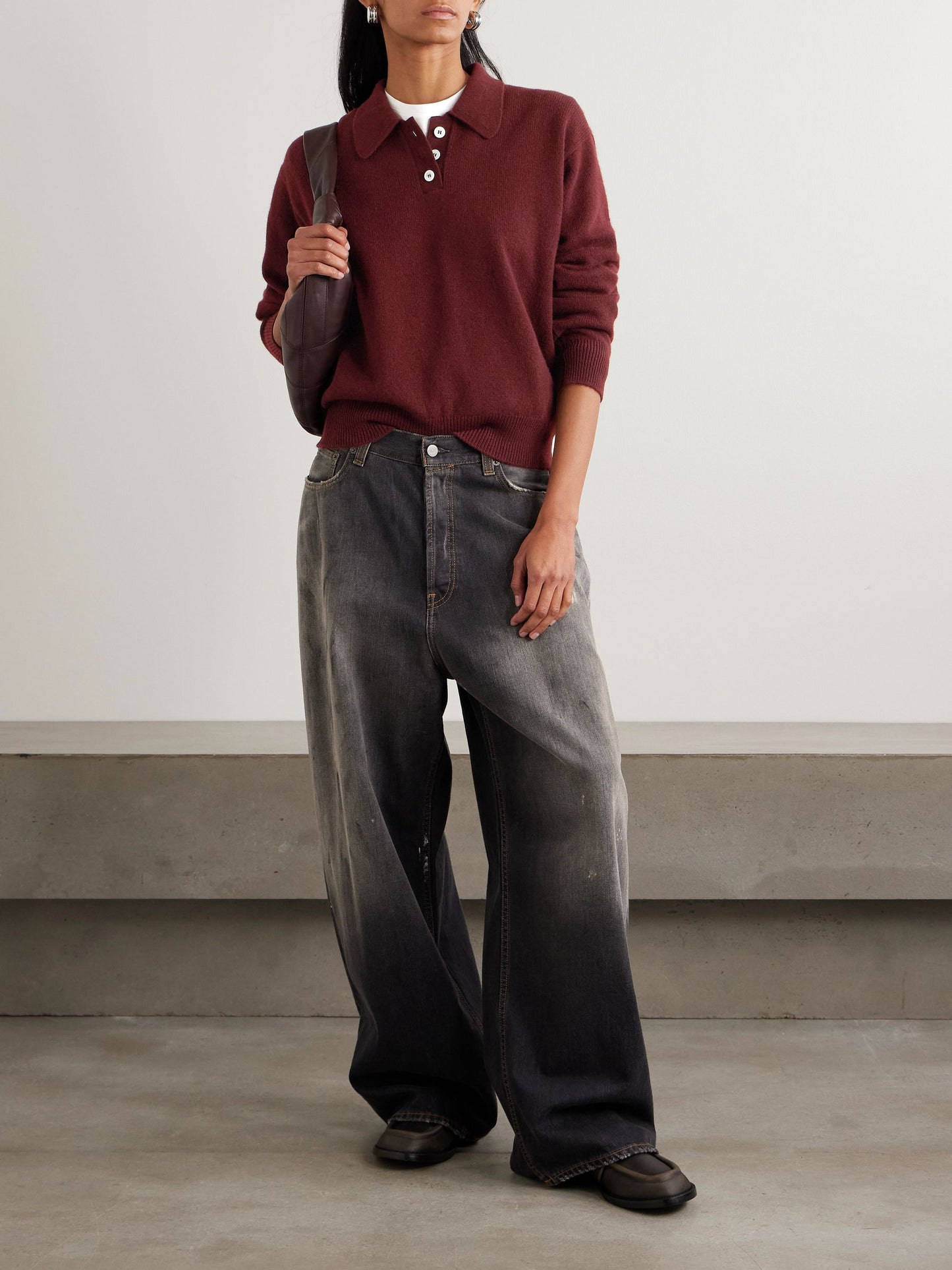 Person wearing a burgundy sweater and black jeans against a plain background