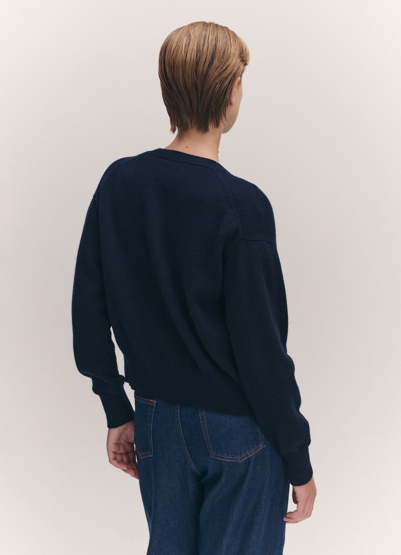 Person wearing a navy sweater and blue jeans against a plain background