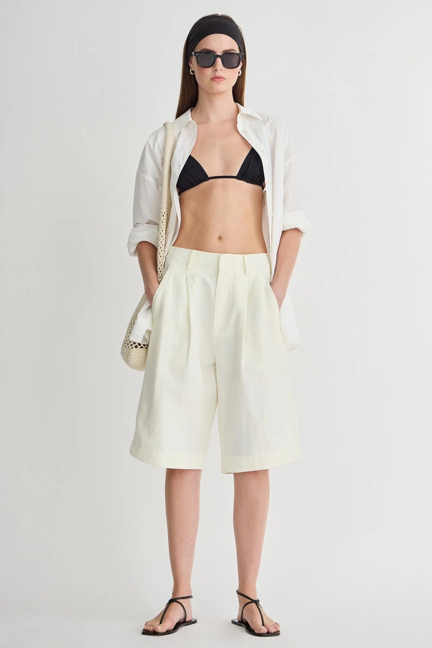 Woman wearing a white shirt, black bikini top, light yellow shorts, and black sandals on a white background