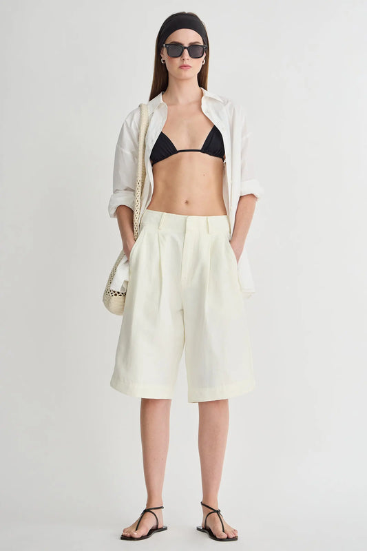 Woman wearing a white shirt, black bikini top, light yellow shorts, and black sandals on a white background