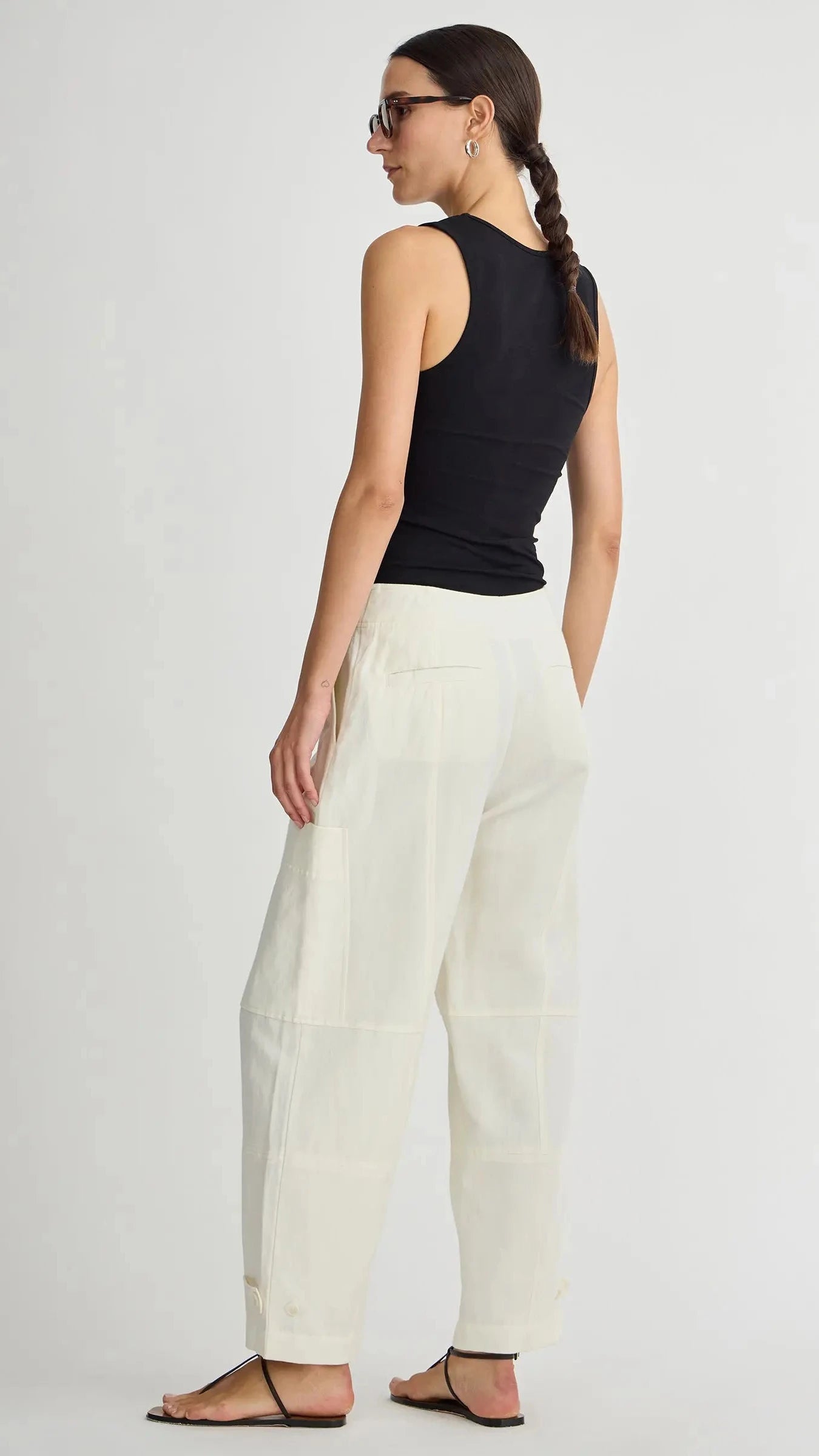 Woman wearing a black sleeveless top and white pants on a plain background