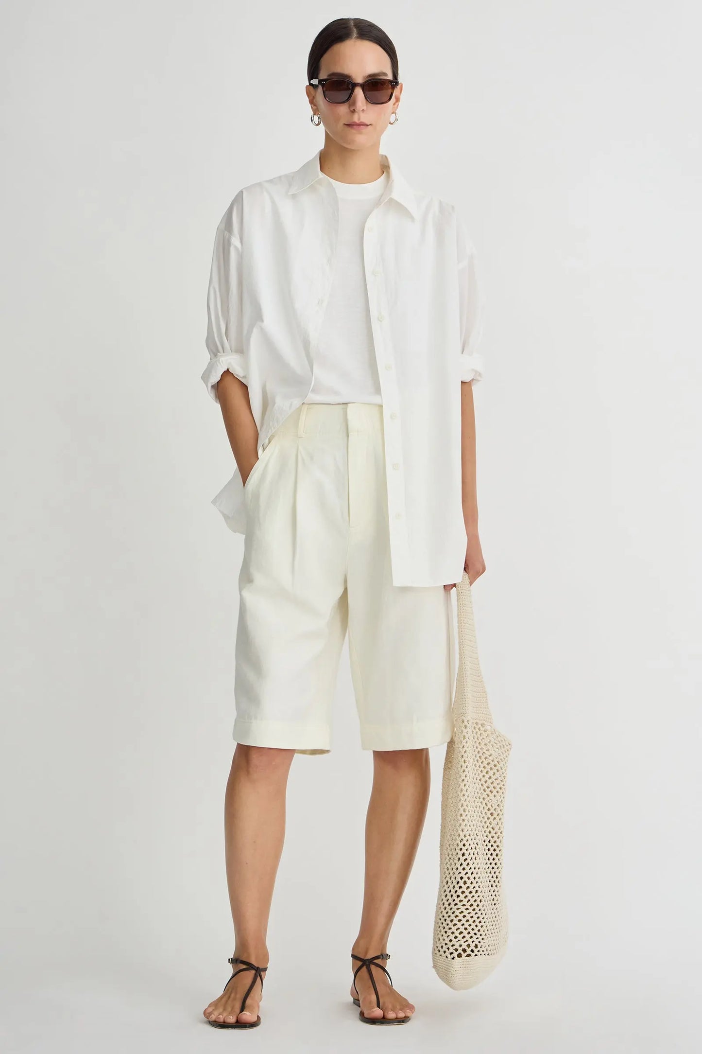 Person wearing a white outfit with sunglasses and a mesh bag on a plain background
