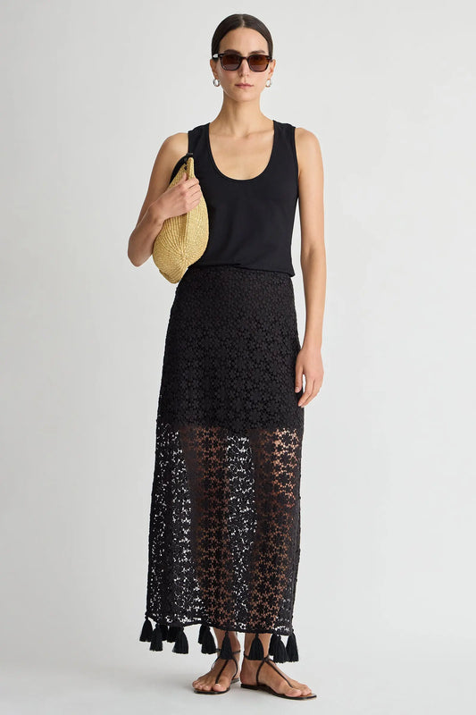 Woman wearing a black sleeveless top and black lace skirt holding a yellow handbag on a light gray background
